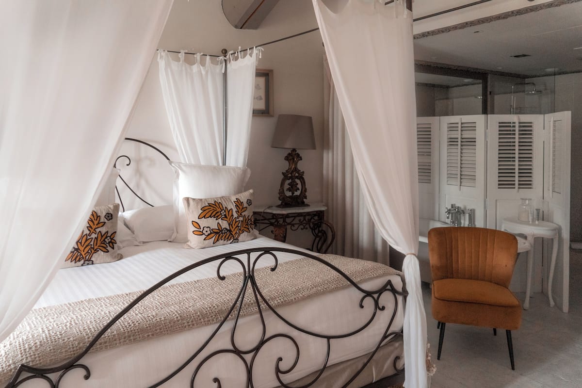 A bedroom with a canopy bed, a bedside table with a lamp, and a chair.