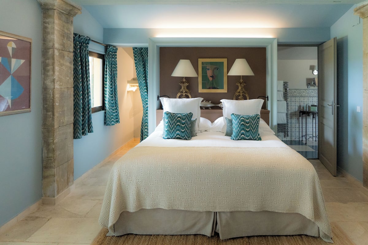 A spacious bedroom with a large bed, two bedside lamps, and a view into the adjacent bathroom.