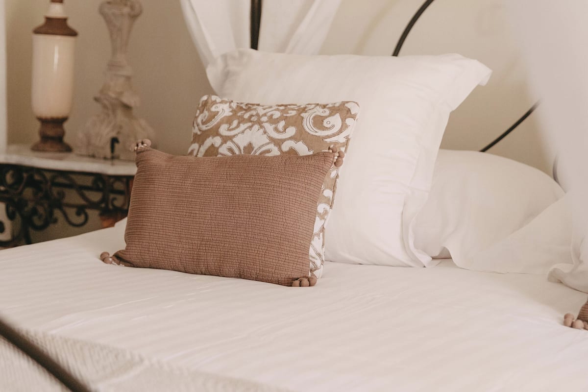 A bed with white bedding and a brown pillow, a nightstand with a lamp, and a decorative item.