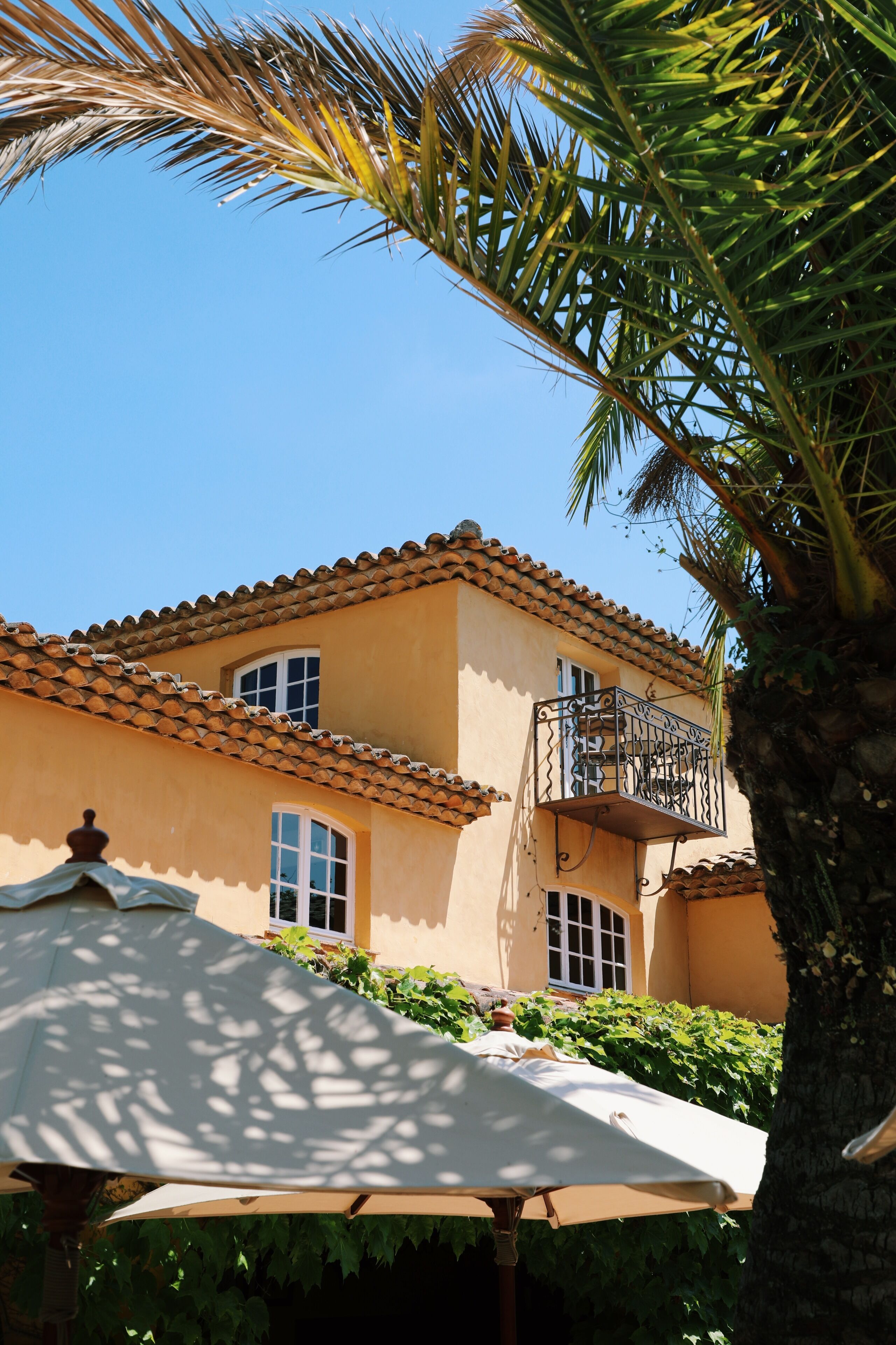 A building with a tiled roof, a balcony with a wrought iron railing, and a white umbrella.