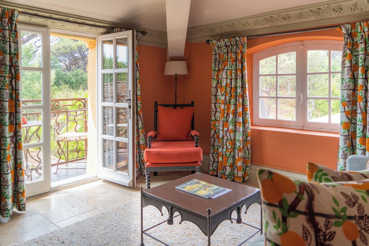 A room with a red armchair, a table with a book, and a view of the outdoors through a glass door.