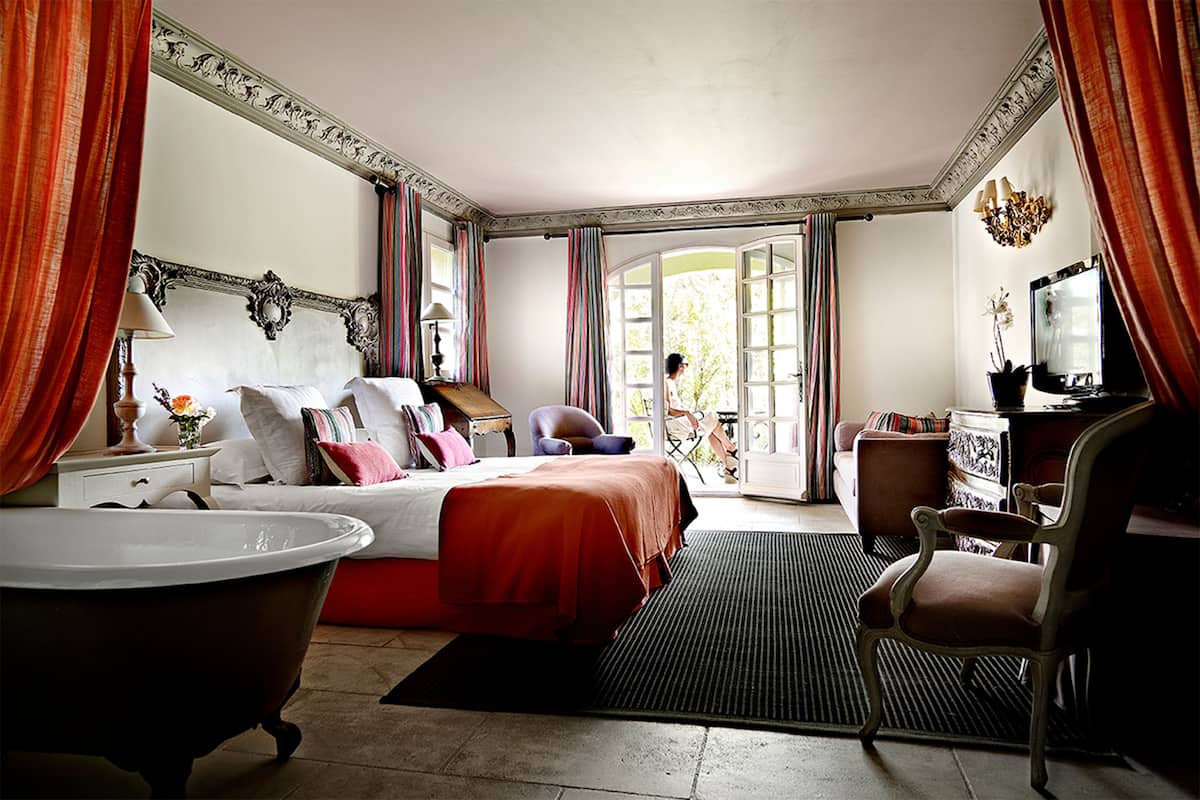 A hotel room with a large bed, a sitting area with a chair, a desk, a television, and a bathtub.