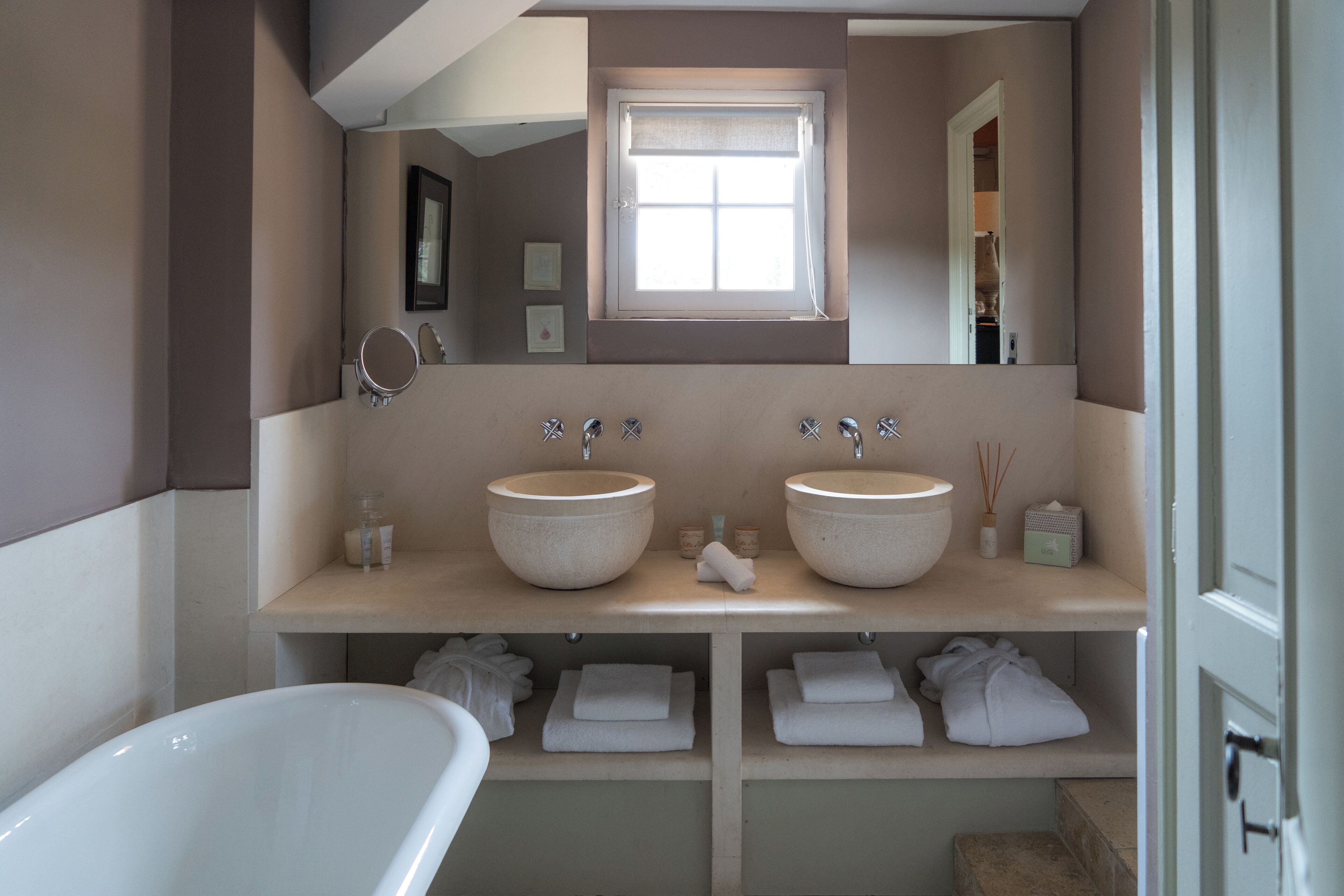Un baño con dos lavamanos, una bañera y una ventana sobre los lavamanos.