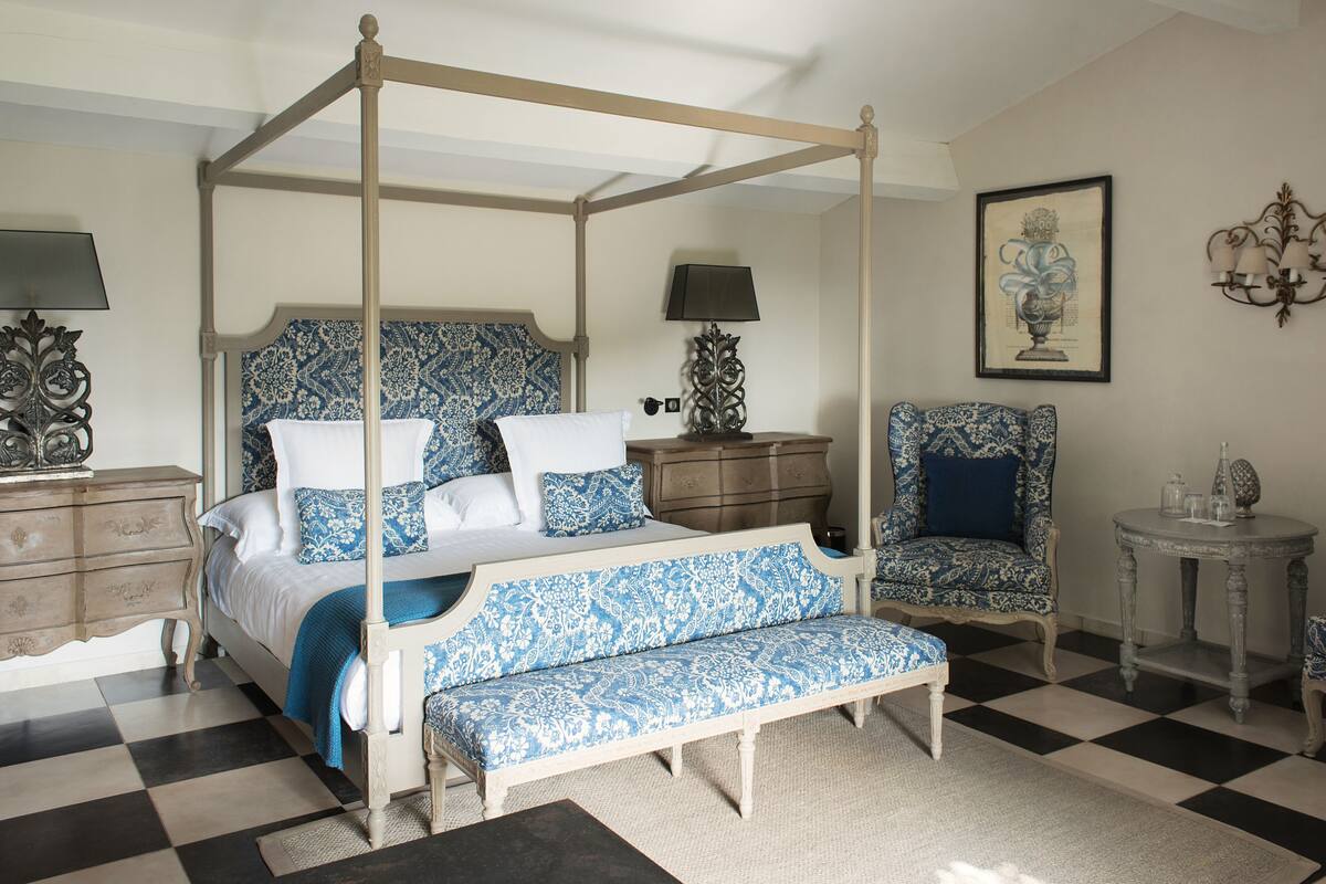 A four-poster bed with a matching bench, a chair, and a small table with a lamp.