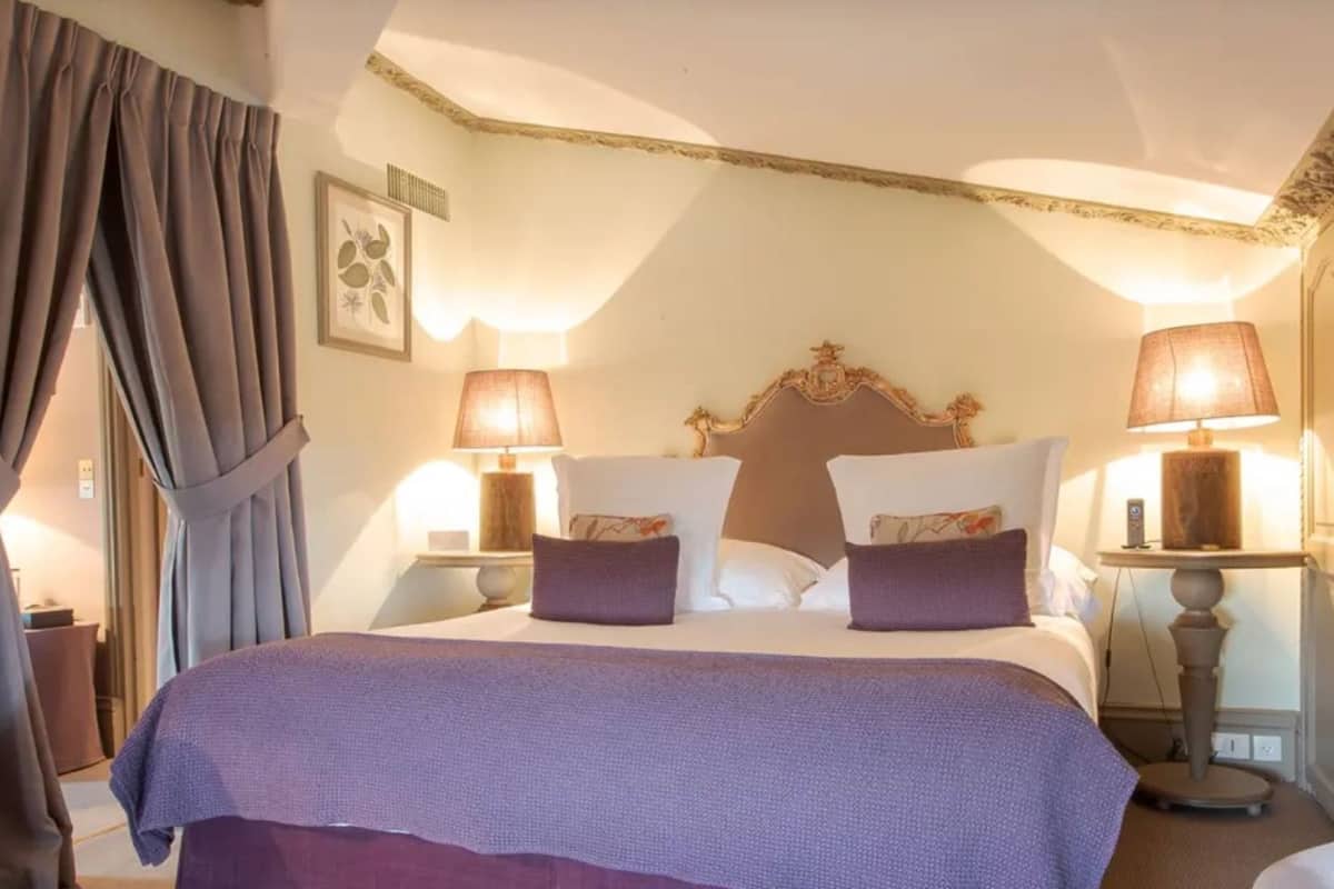 A hotel room with a large bed, two bedside lamps, a headboard, and a door.