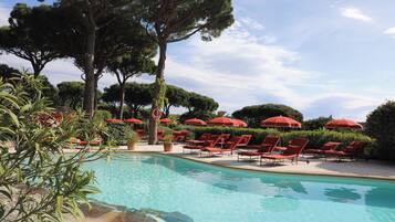 A pool area with red lounge chairs and umbrellas, surrounded by trees and greenery.