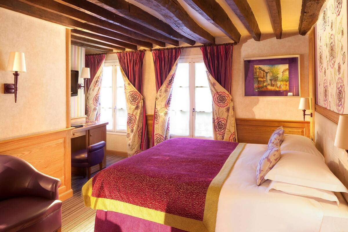 A hotel room with a bed, a desk, a chair, and a window with curtains.