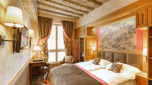 A hotel room with a large bed, a desk, a chair, and a window with curtains. - Hotel La Perle (Paris)