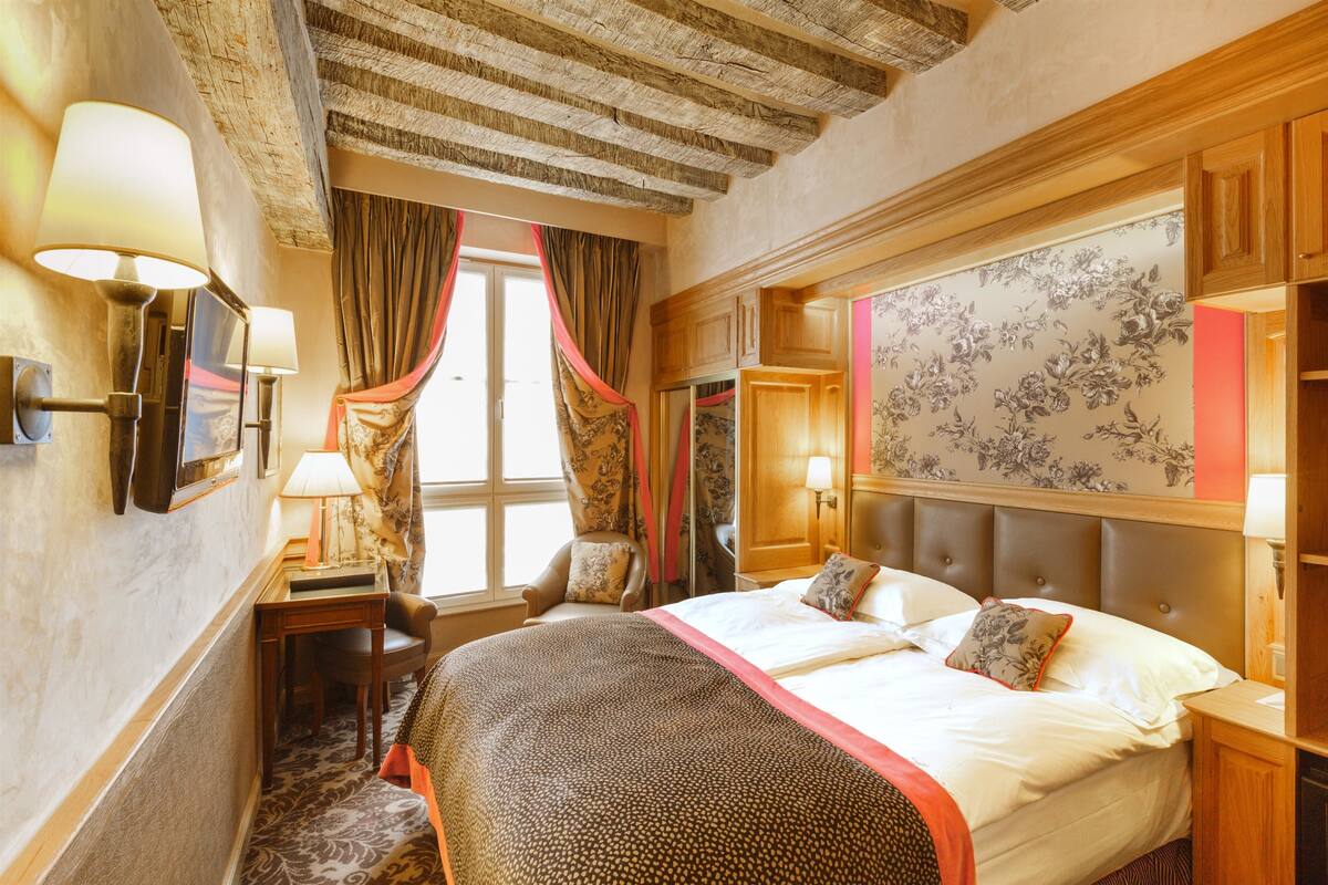 A hotel room with a large bed, a desk, a chair, and a wardrobe.