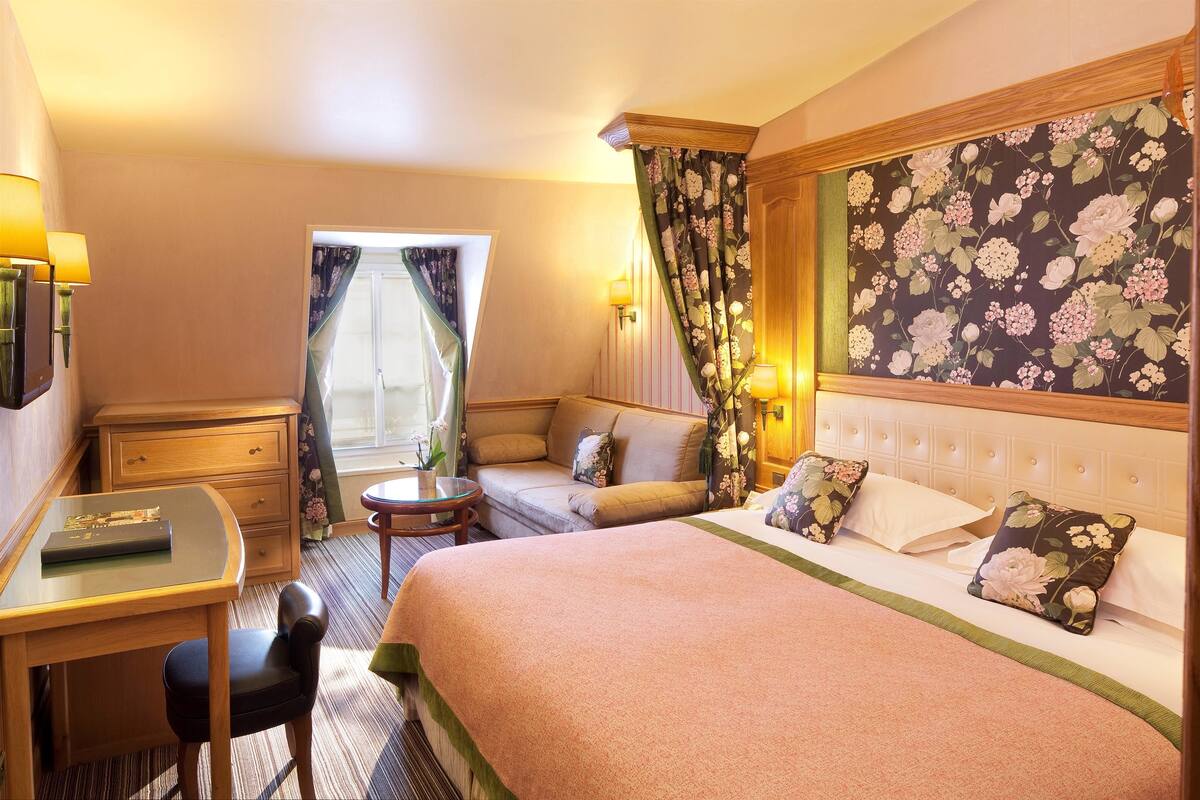 A hotel room with a bed, a desk, a chair, a small table, and a sofa.