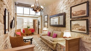 A cozy room with a stone wall, a sofa with cushions, a table, wicker chairs, and framed pictures on the wall. - Hotel La Perle (Paris)