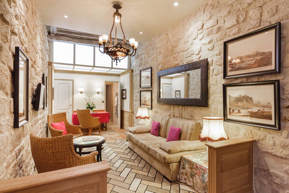 A cozy room with a stone wall, a sofa with cushions, a table, wicker chairs, and framed pictures on the wall.