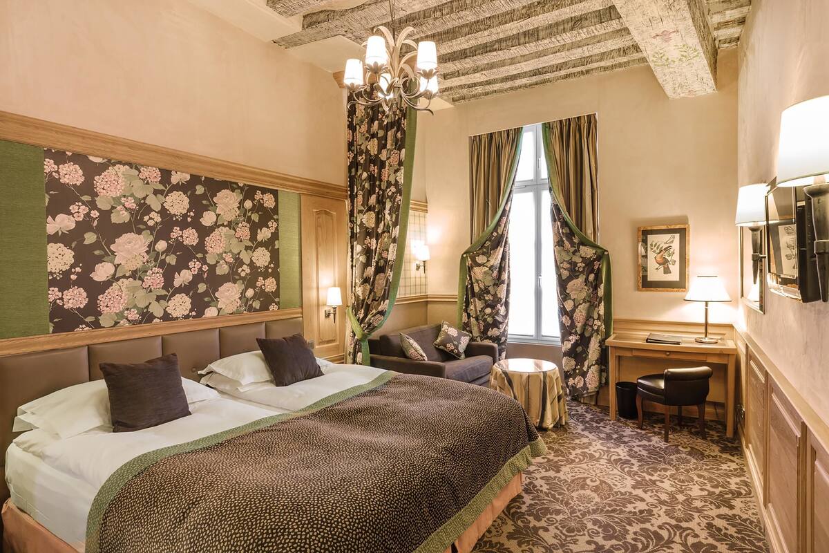 A hotel room with a large bed, a desk, a chair, a small table, and a window with curtains.