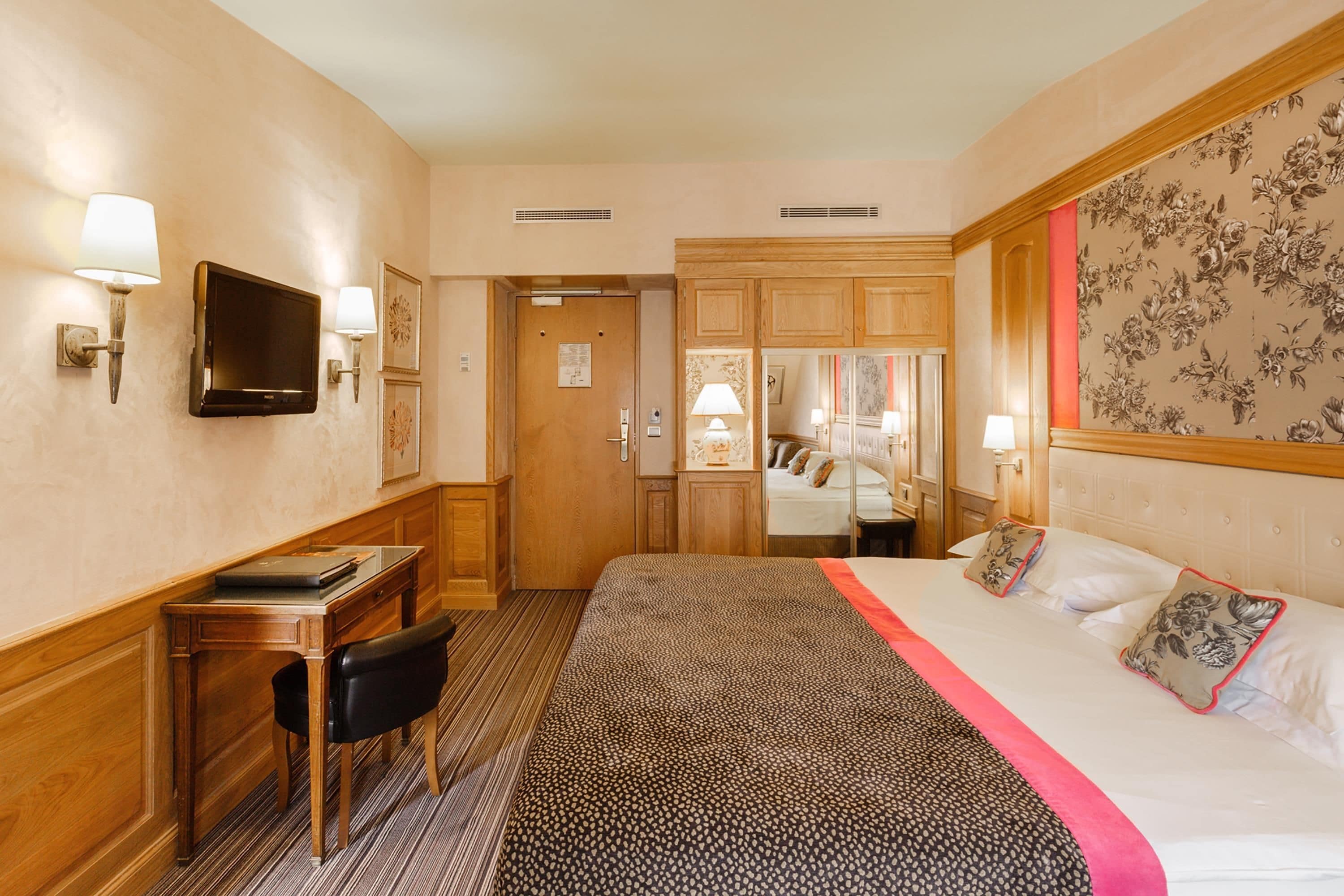 Ein Hotelzimmer mit Bett, Schreibtisch, Stuhl, Fernseher und einer Tür zu einem Badezimmer.