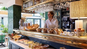A breakfast buffet with various food items, including bread, pastries, and eggs, in a well-lit room with a coffee machine and wine glasses on display. - Hotel La Perle (Paris)