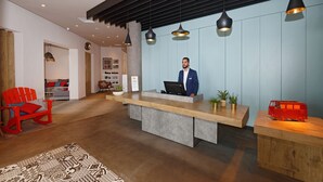 A reception area with a wooden reception desk, a red rocking chair, and a red toy van. - Hotel ibis El Jadida (El Jadida)