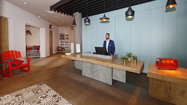 A reception area with a wooden reception desk, a red rocking chair, and a red toy van. - Hotel ibis El Jadida (El Jadida)