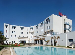Un hotel con piscina, mobiliario exterior y un cielo azul despejado.