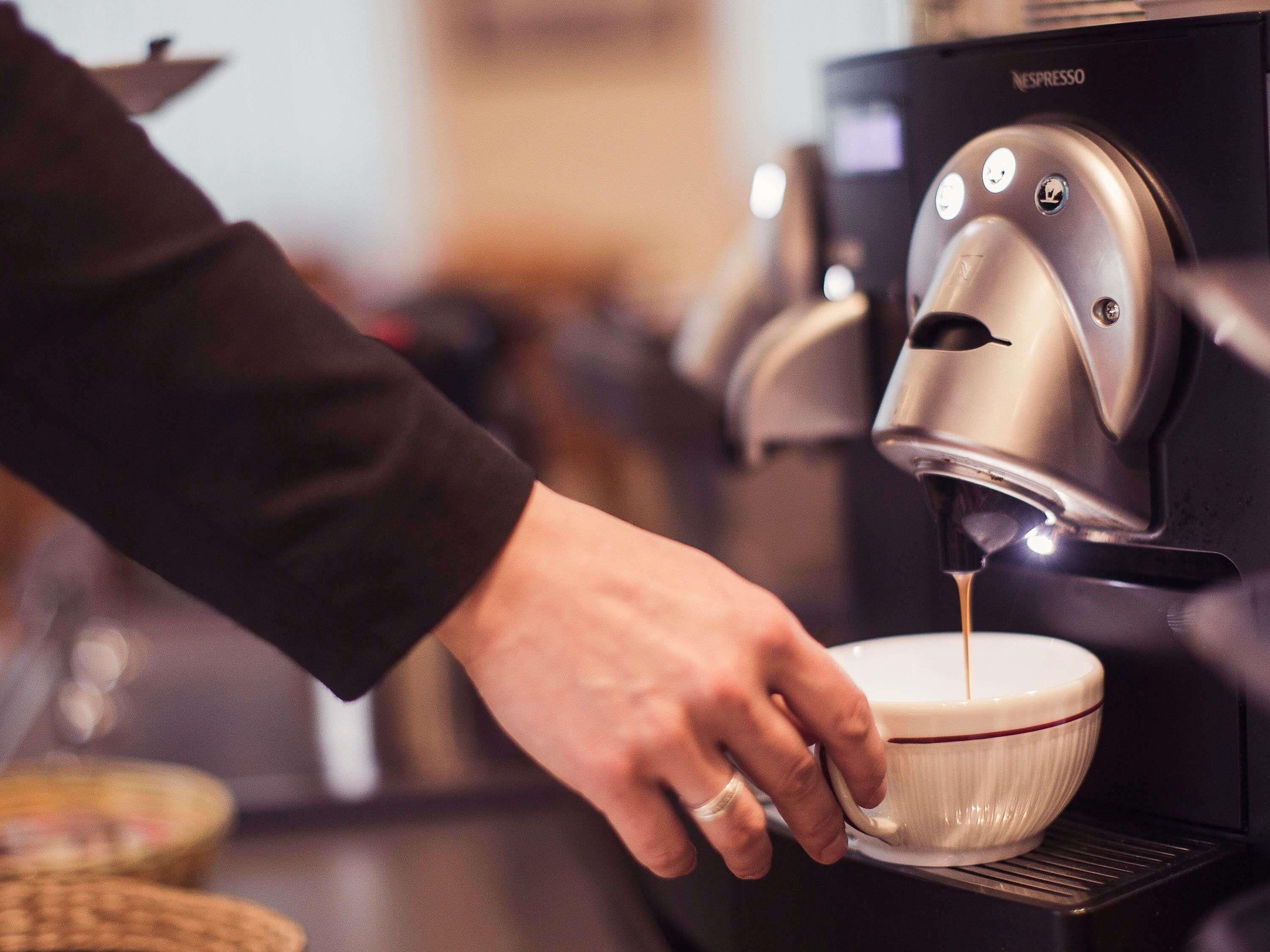 En hand håller en kopp under en kaffemaskin som brygger espresso.