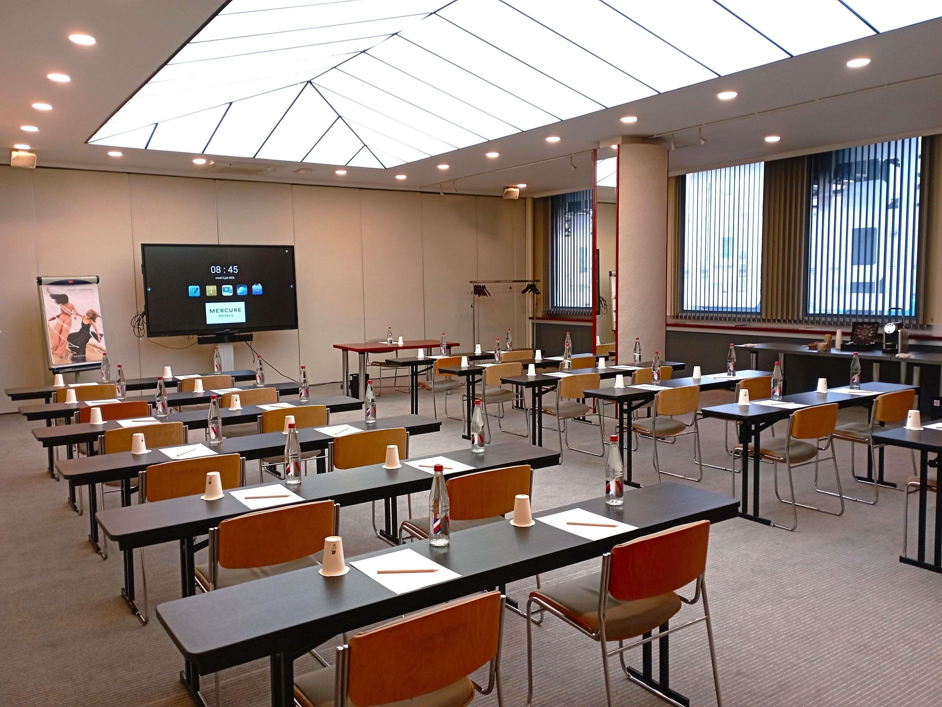 Un salón de conferencias con mesas, sillas, una pantalla de proyector y un ventanal grande.