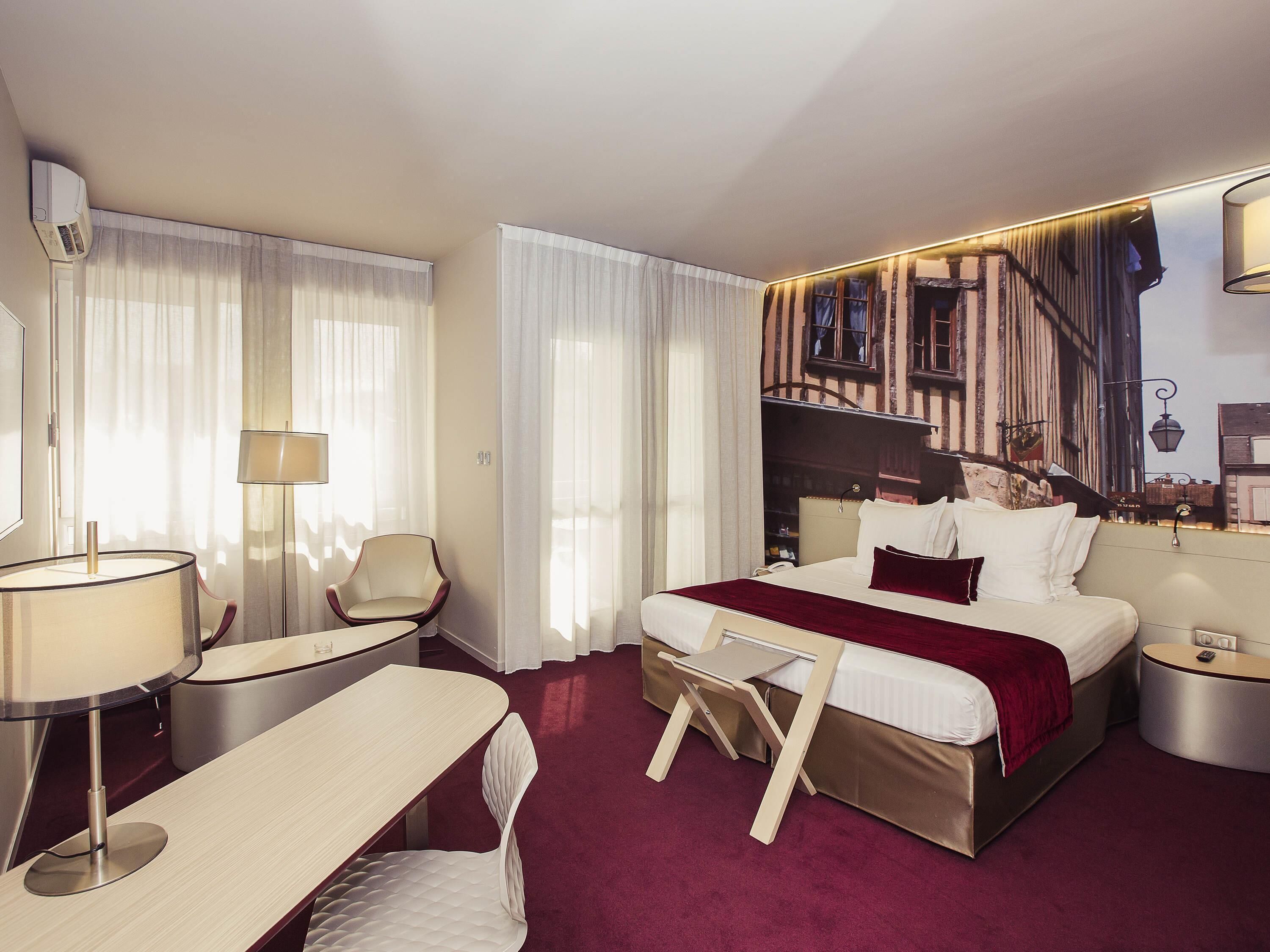 A hotel room with a bed, a desk, a chair, a lamp, and a wall-mounted air conditioner.