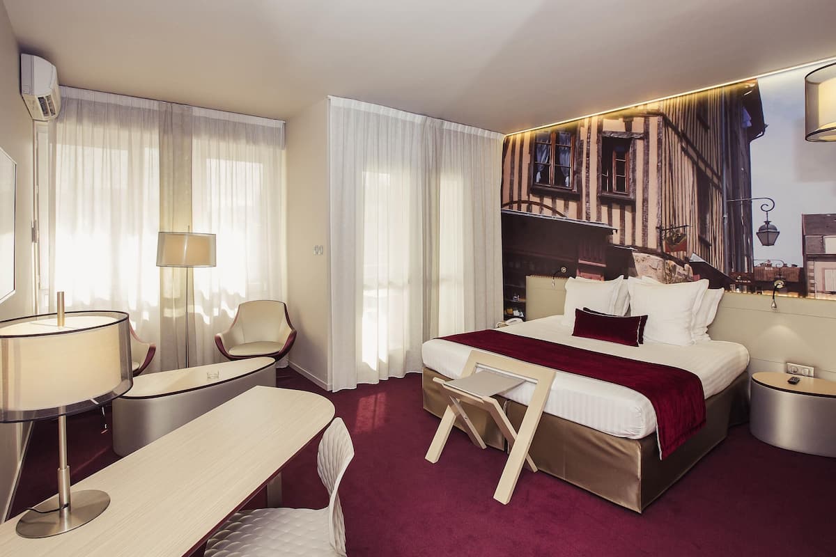 A hotel room with a bed, a desk, a chair, a lamp, and a wall-mounted air conditioner.