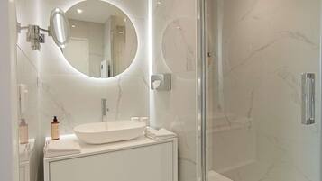 Un baño moderno con cabina de ducha de vidrio, un espejo redondo y un tocador blanco.