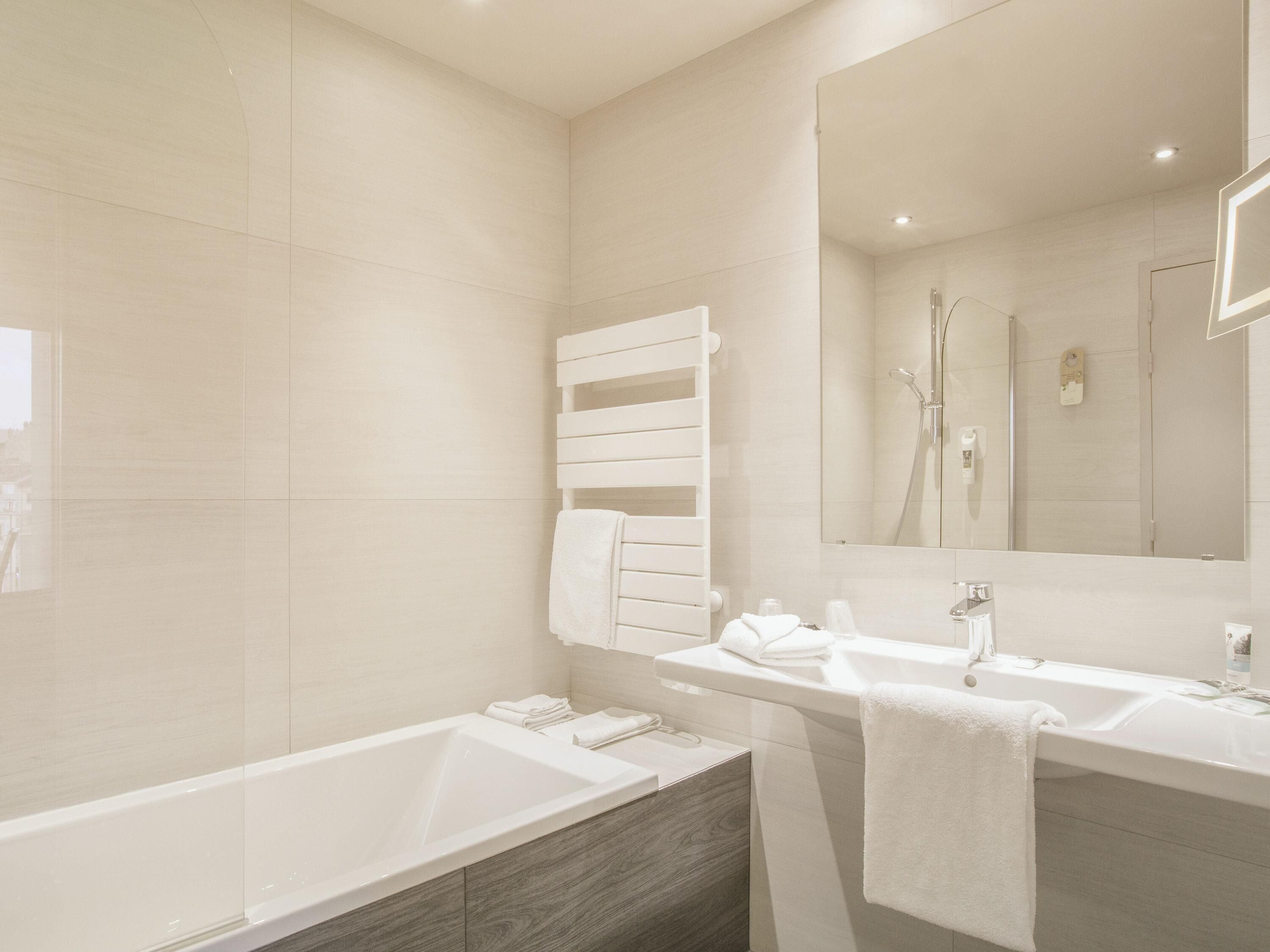 A modern bathroom with a bathtub, a sink, a mirror, and a towel rack.