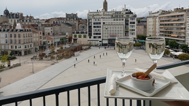 A balcony with a tray holding two wine glasses and a dessert bowl, overlooking a cityscape with historic buildings and a prominent church spire. - Hôtel Mercure Limoges Centre (Limoges)