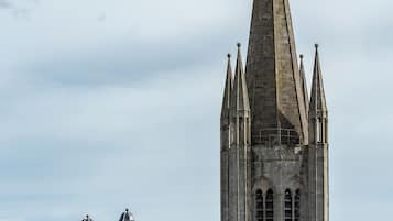 Una iglesia histórica con una alta aguja y dos torres abovedadas, frente a un cielo nublado.