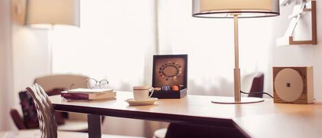 A modern room with a dining table, chairs, a lamp, a small table with a cup and books, and a decorative item.