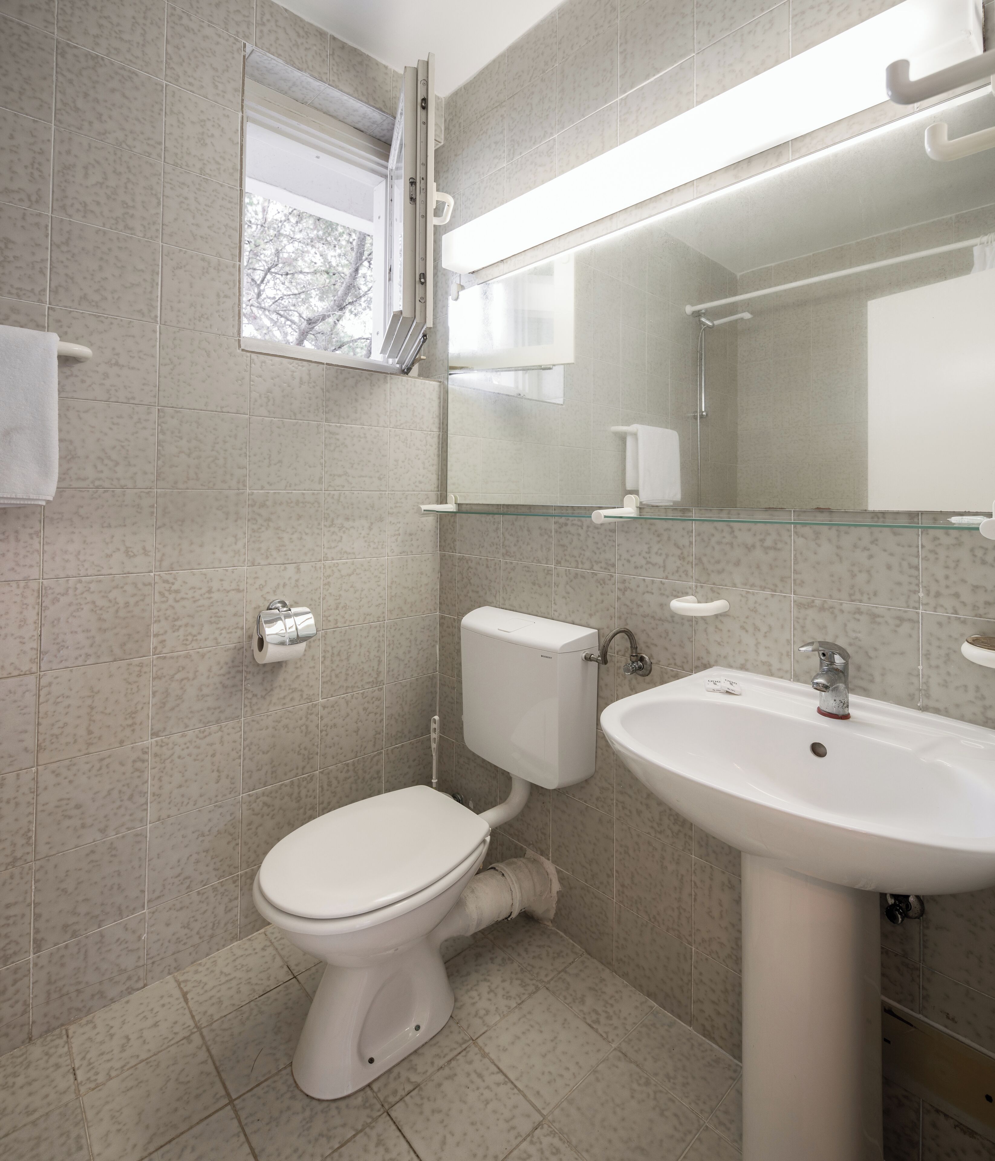 Une salle de bain avec des toilettes, un lavabo et une fenêtre située au-dessus des toilettes.