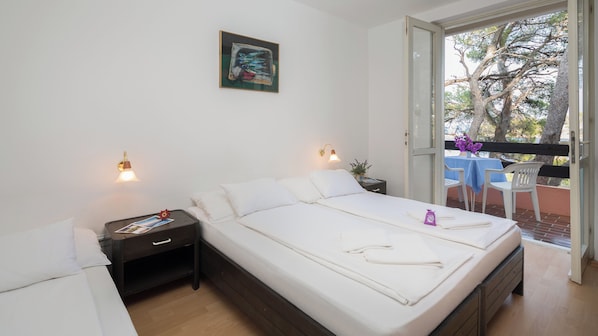 A bedroom with a bed, bedside tables, a nightstand, a painting on the wall, and a balcony with a table and chairs. - Resort Fontana (Jelsa)