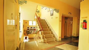 Vestíbulo de hotel con una escalera, una recepción y un letrero que indica el segundo piso.