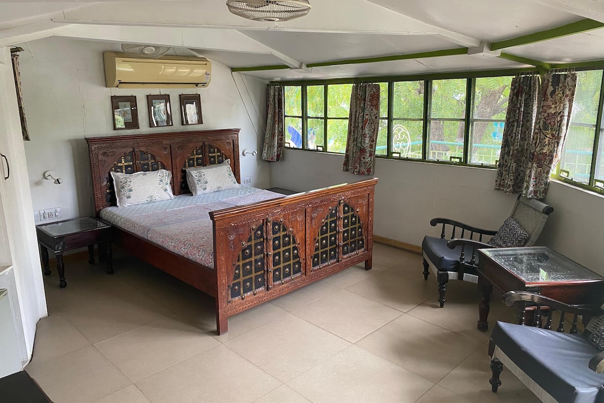 A bedroom with a wooden bed, a small table, a chair, and a window with curtains.