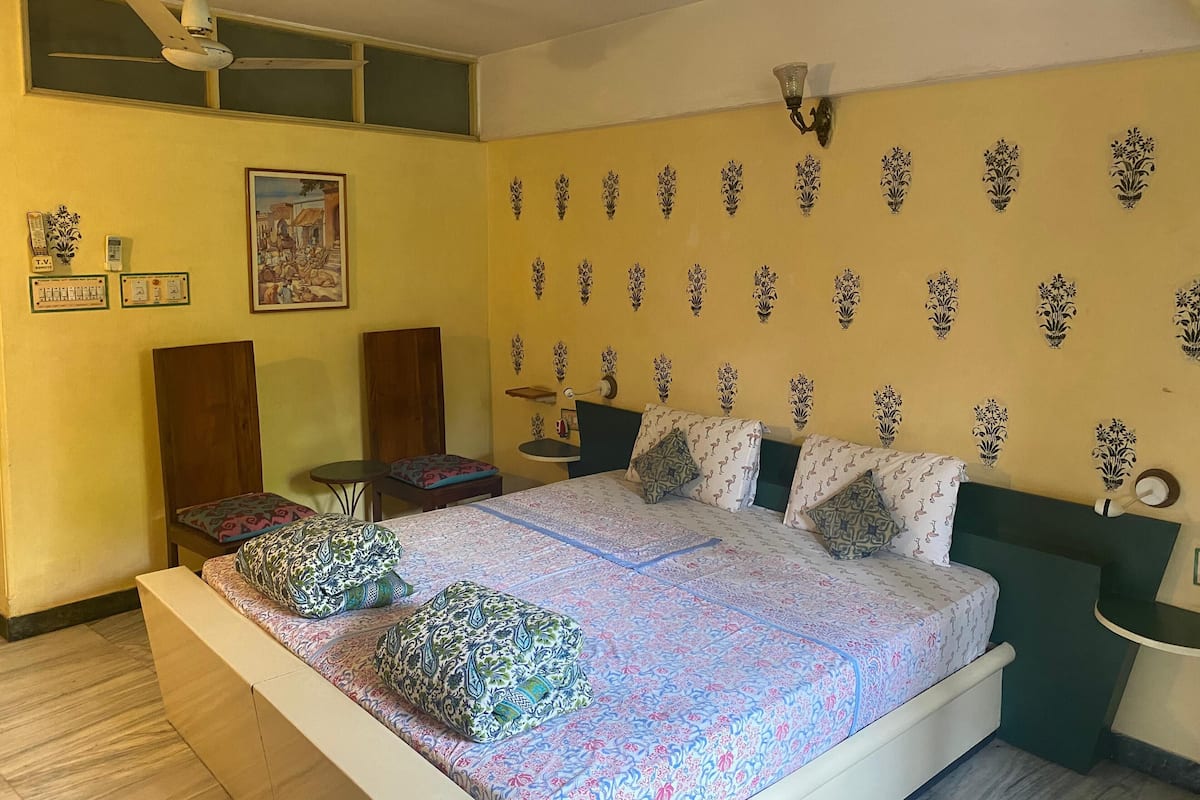 A bedroom with a bed, pillows, a nightstand, a wall-mounted lamp, and a ceiling fan.