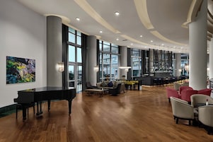 A spacious lobby with a grand piano, comfortable seating, a bar area, and large windows offering views.