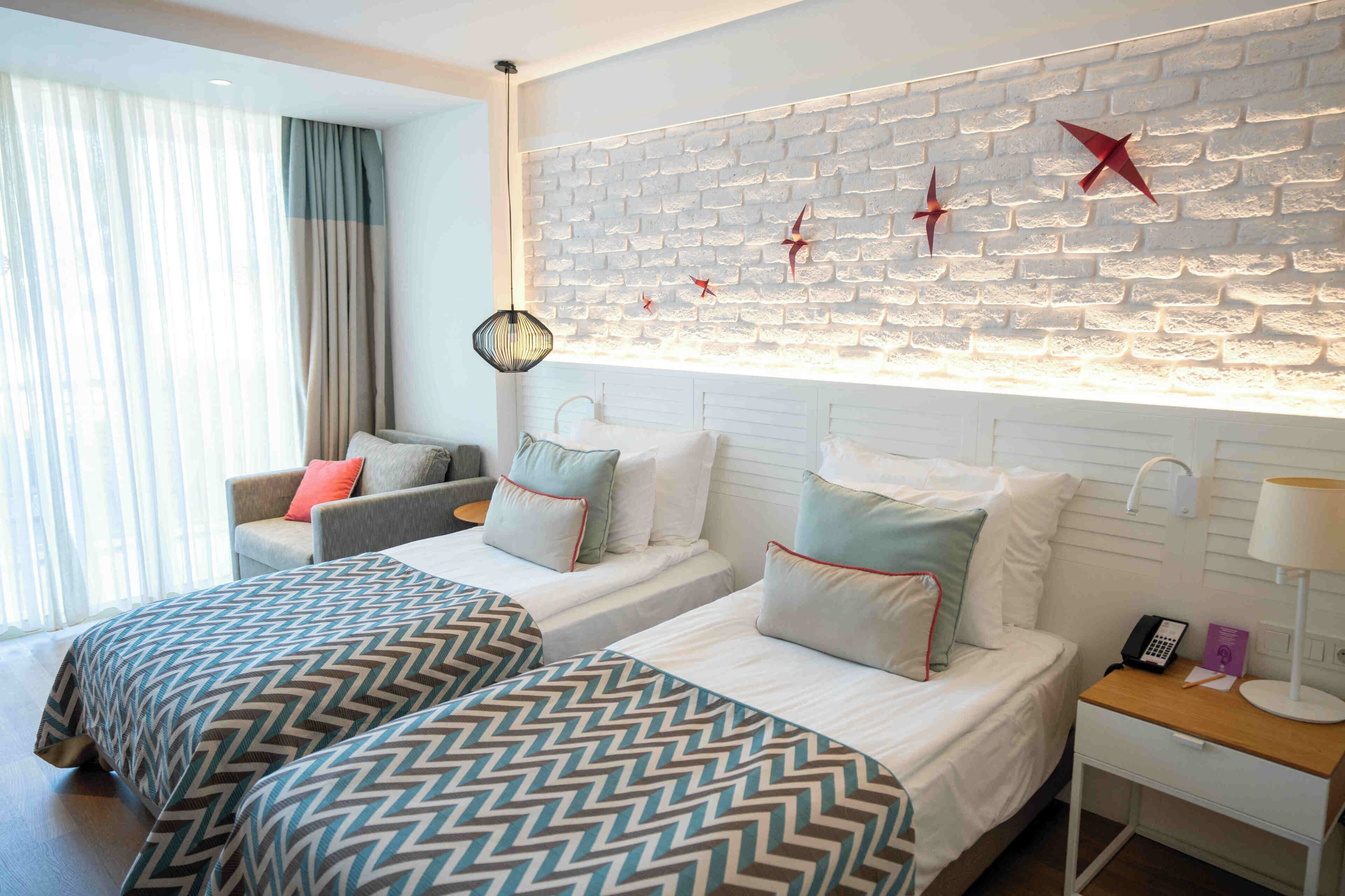 A hotel room with two beds, a sofa, a nightstand, a lamp, and a decorative wall with brick pattern and red stars.