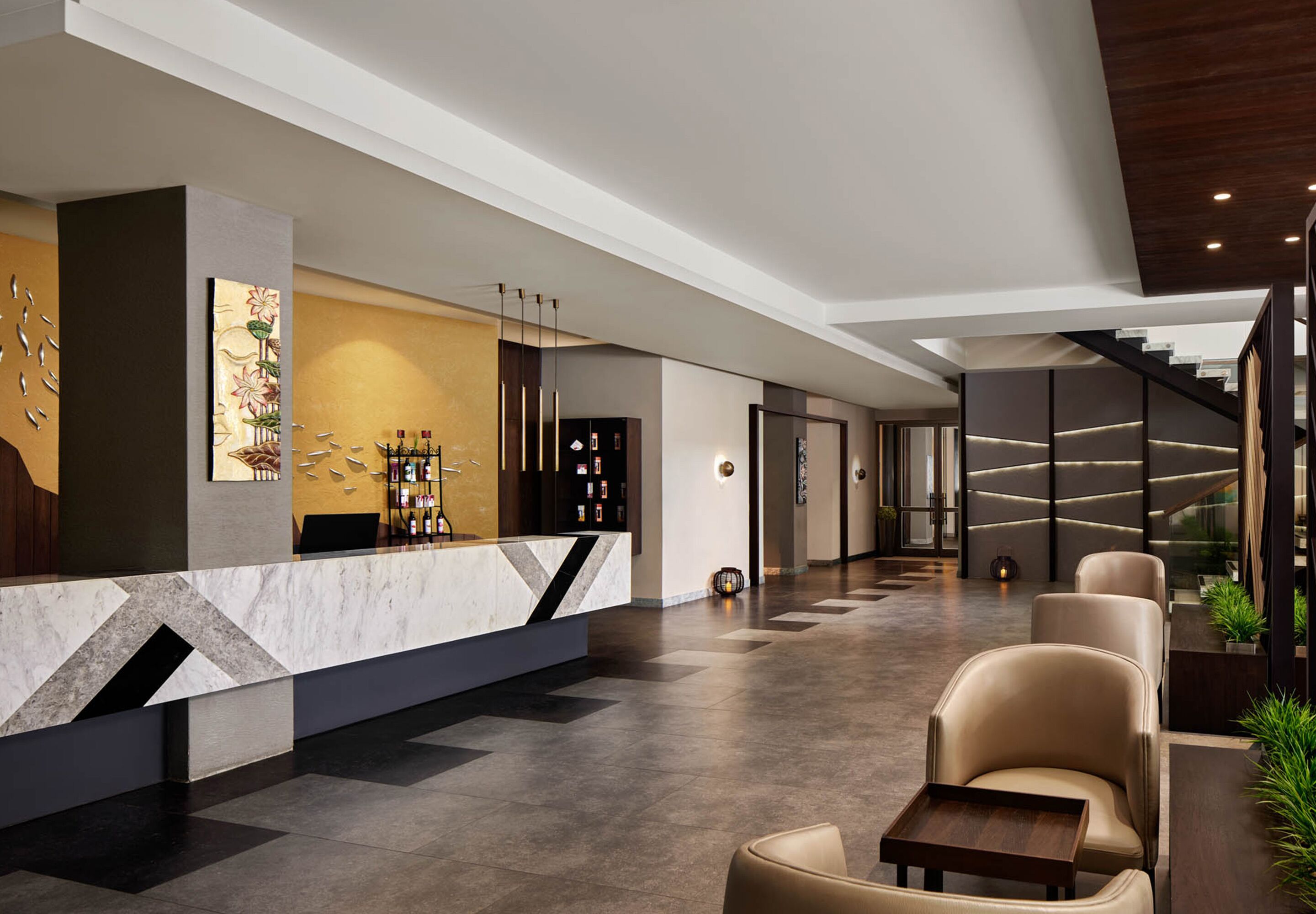 A modern lobby with a reception desk, seating area, and a staircase.