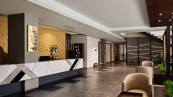A modern lobby with a reception desk, seating area, and a staircase.