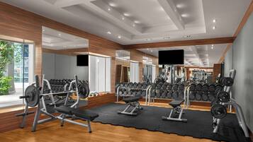 Une salle de sport équipée de matériel de musculation, de miroirs et d’une grande fenêtre donnant sur l’extérieur.