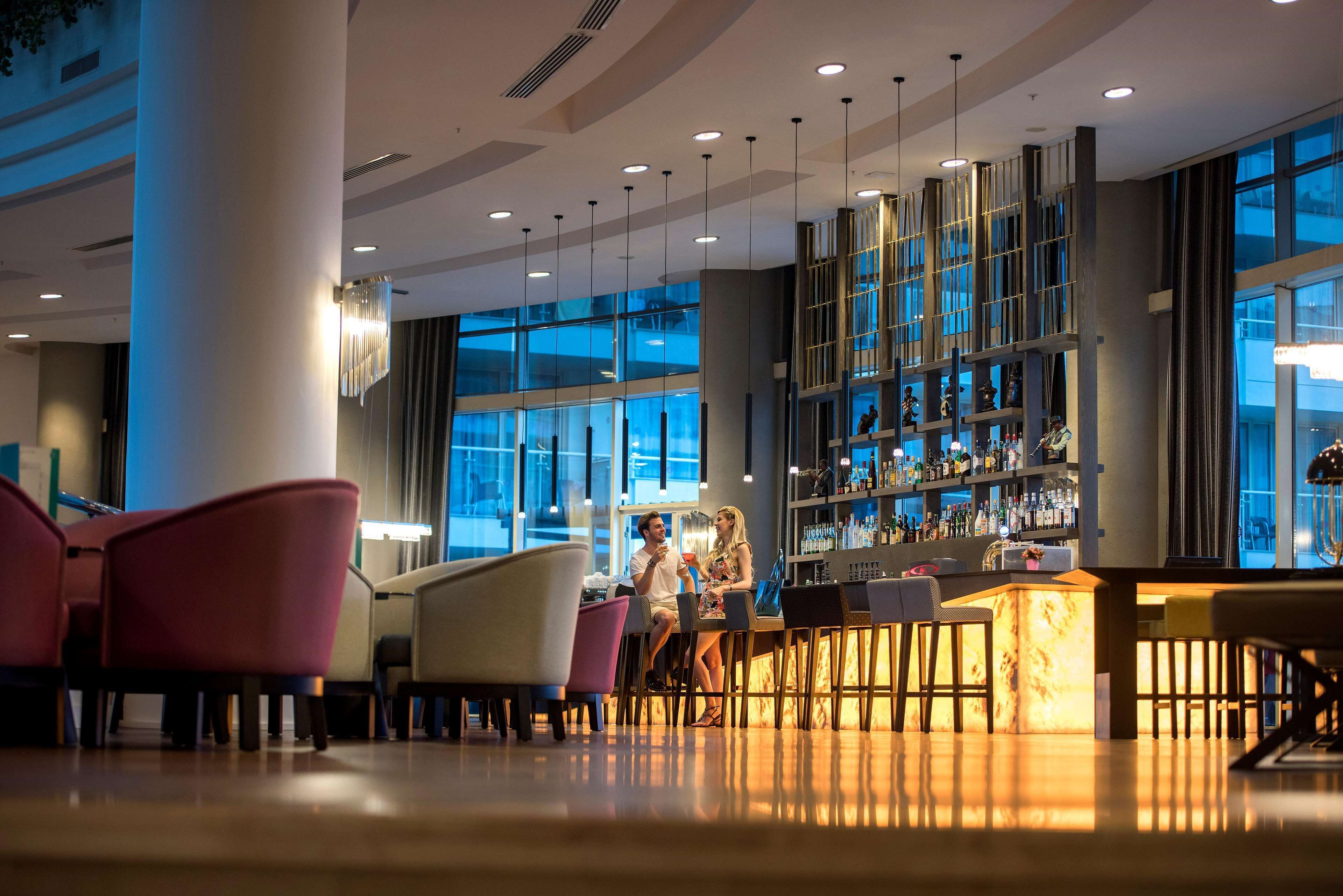 A modern bar area with seating, a bar counter, and a large window providing a view of the outside.