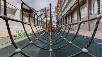 Estructura de escalada con cuerdas en un espacio al aire libre, con edificios al fondo.
