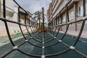 Estructura de escalada con cuerdas en un espacio al aire libre, con edificios al fondo.