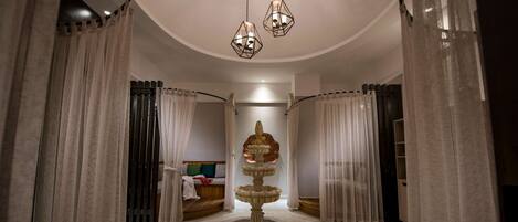 Amplia habitación con una fuente central, cortinas blancas y una cama con cabecero.