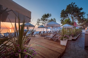 Une terrasse en bois, dotée de chaises longues et de parasols, qui offre une vue sur une étendue d’eau.