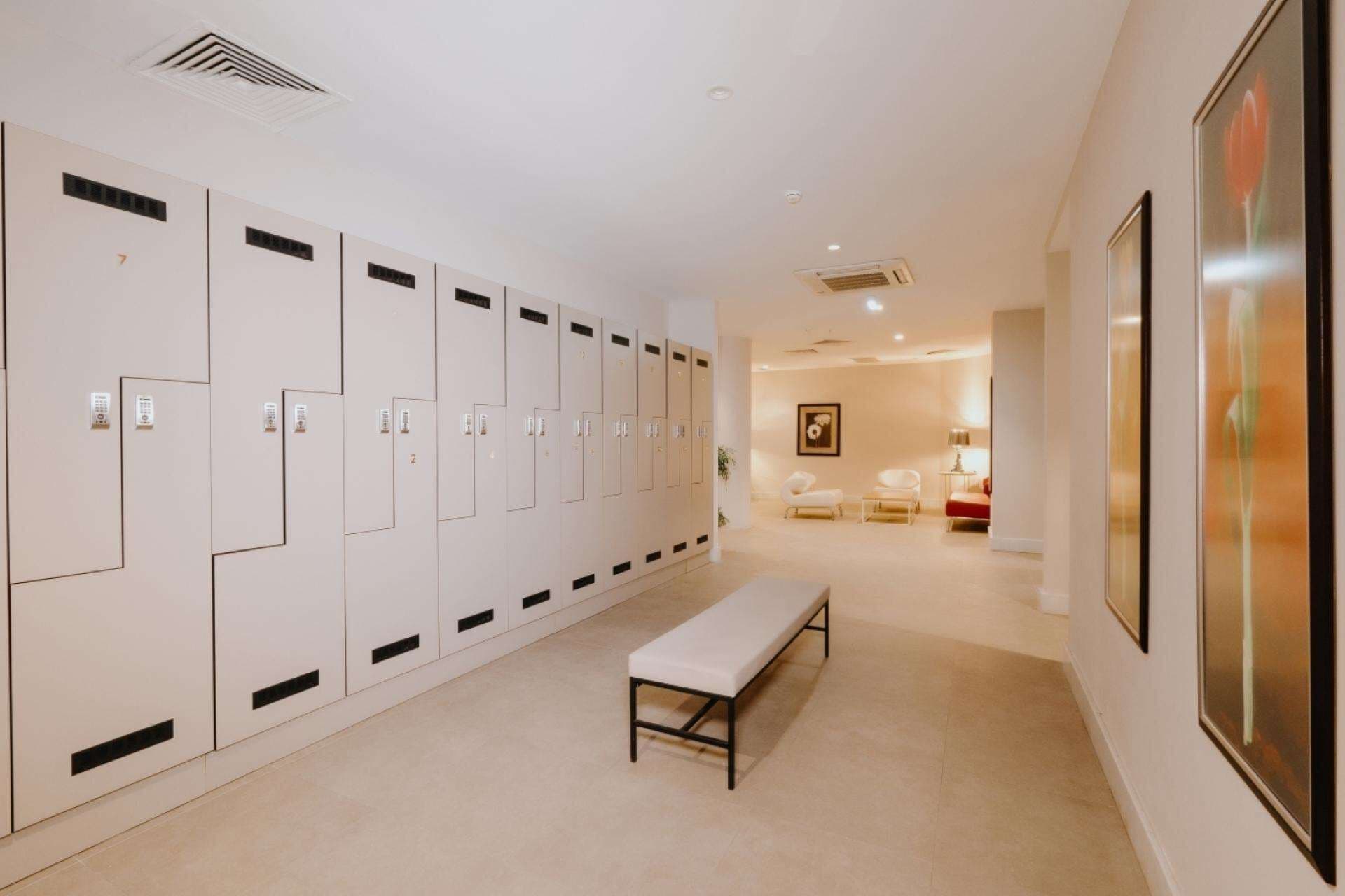 A hallway with lockers, a bench, and a framed picture on the wall.