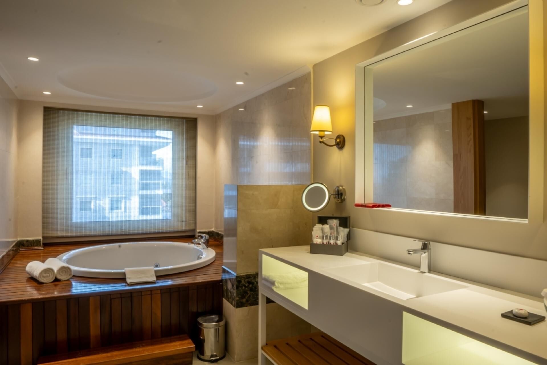 Un baño moderno con una bañera grande, dos lavamanos, un espejo y una ventana con persianas.