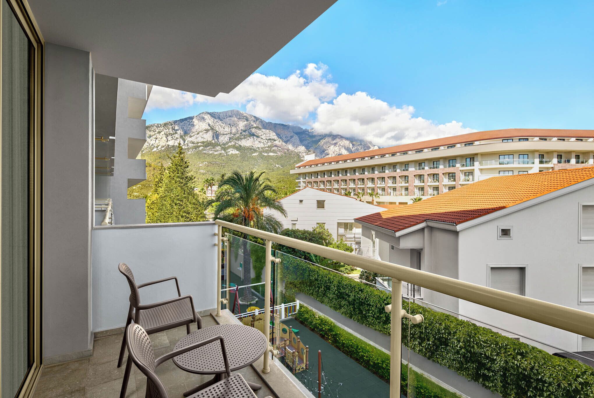 A balcony with a view of a mountain, a playground, and a building with a red roof.