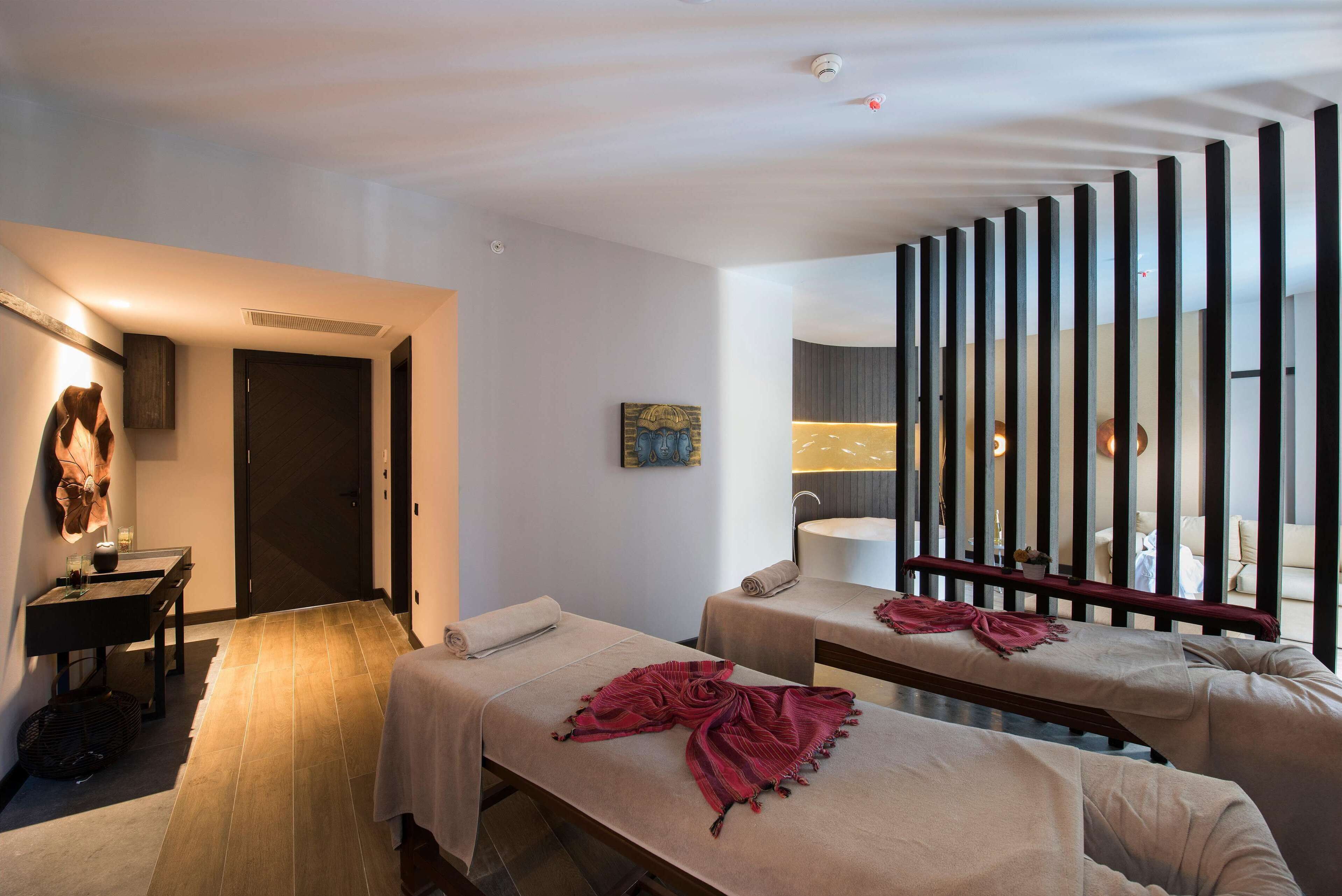 Habitación de hotel con dos camas, zona de estar, escritorio y un ventanal grande con persianas.